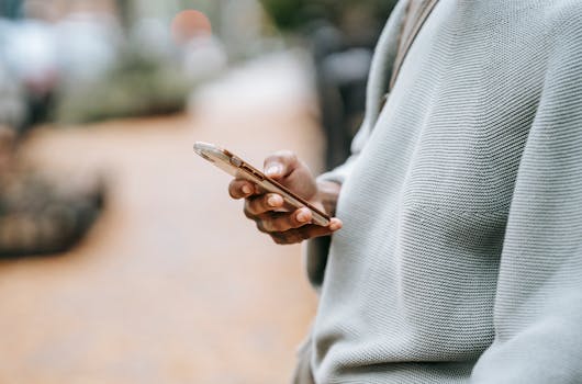 A person casually uses a smartphone outdoors in an urban environment, focusing on connection.