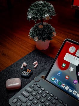 A stylish desktop setup featuring an iPad, keyboard, earbuds, and decorative plant.