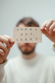 Blurred image of a man holding a card with the phrase 'Sorry Not Sorry'.