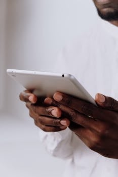 Professional holding a tablet, focusing on hands and technology in a bright setting.