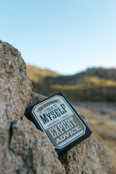 Close-up of an inspirational quote box nestled among rocks in a scenic outdoor landscape.